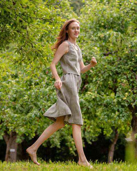 In this photograph the model is wearing the matching crop top and skirt set in green gingham. She is captured during a movement, while she is running - her hands and feet are in a relaxed position and she is slightly above the ground. The picture highlights the length of the garments.
