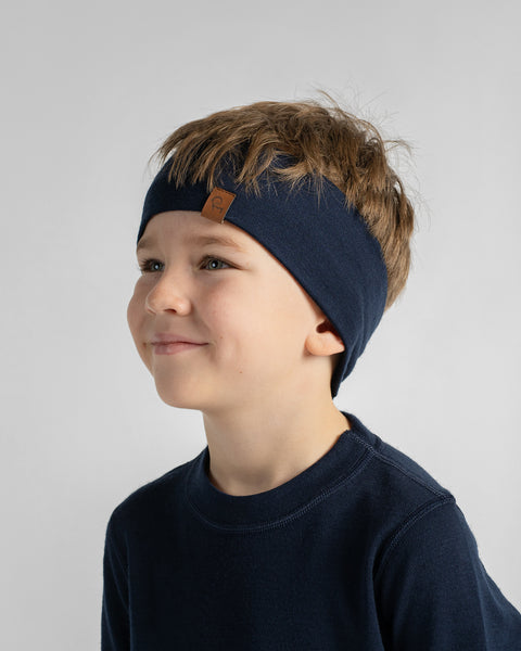 A young boy looking sideways and smiling, wearing a dark navy t-shirt and a matching navy knit headband.