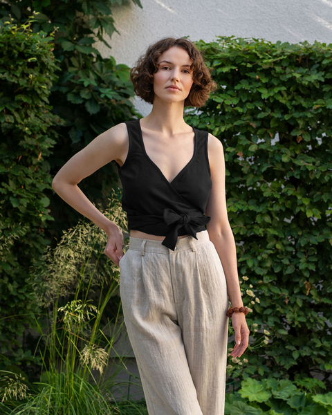 The model is wearing the ARIA linen crop top in pure black color. She is posing facing the camera.