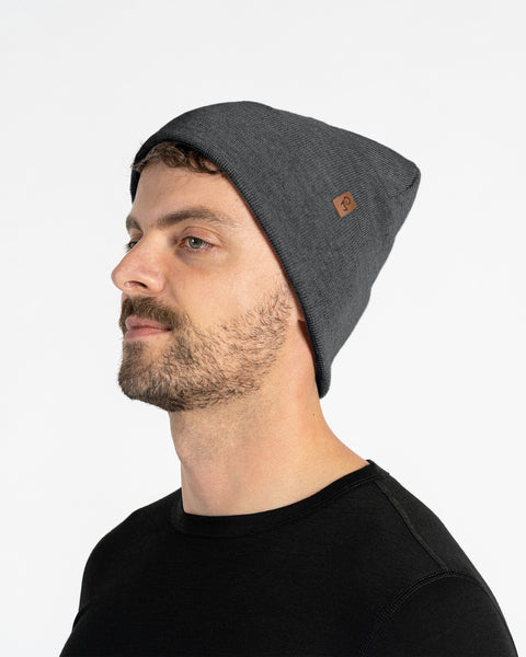 Man in side profile wearing a dark gray merino wool knit beanie with leather logo patch on cuff, studio background