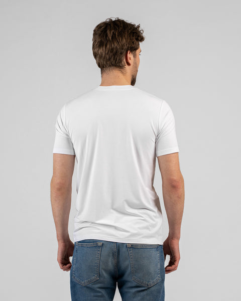 A studio shot showing the back of a man wearing a solid white short-sleeved t-shirt and blue jeans. He is standing facing away from the camera against a plain light grey background.