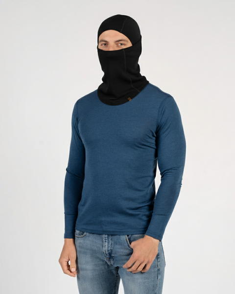Man in blue long-sleeve top wearing a black Merino wool balaclava, shown in a studio setting.