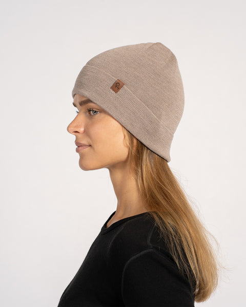 Side profile of woman wearing a creamy beige knitted Merino wool beanie, against light background.
