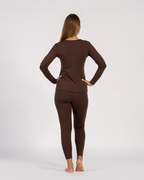 Back view of woman standing barefoot in brown merino wool thermal long sleeve and leggings, hands on hips.