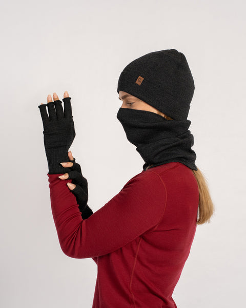 Three-quarter view of a woman in a dark-gray beanie and gaiter, gloves on, arms crossed, with gaiter pulled up over lower face.