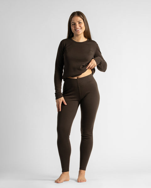 A full-body studio portrait of a woman standing barefoot facing the camera in a dark brown long-sleeve top and matching leggings.