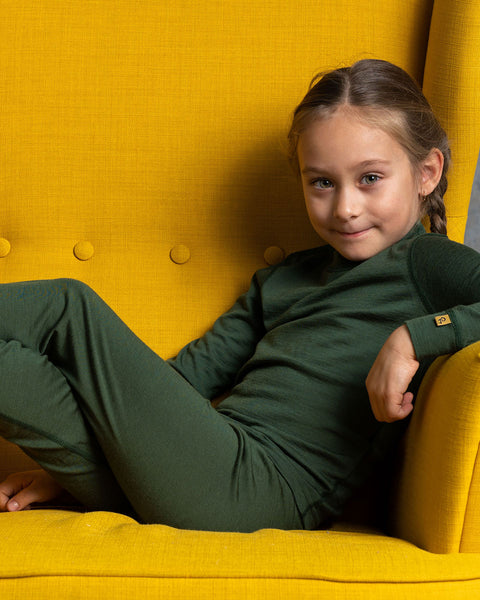 Young girl in a dark green menique outfit sitting on a yellow chair