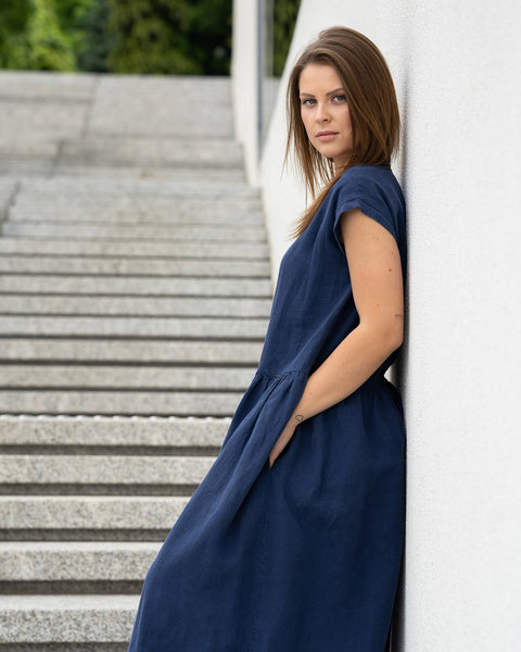Young woman posing in a city street on stears wearing linen smock dress cecilia in a storm blue color.