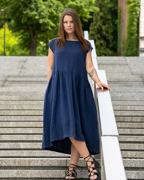 Young woman posing in a city street on stears wearing linen smock dress cecilia in a storm blue color. Girl with a cat tattoo on her left arm.