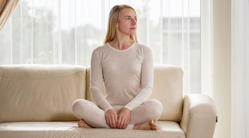 Woman sitting in lotus pose on the sofa and wearing natural merino wool matching set