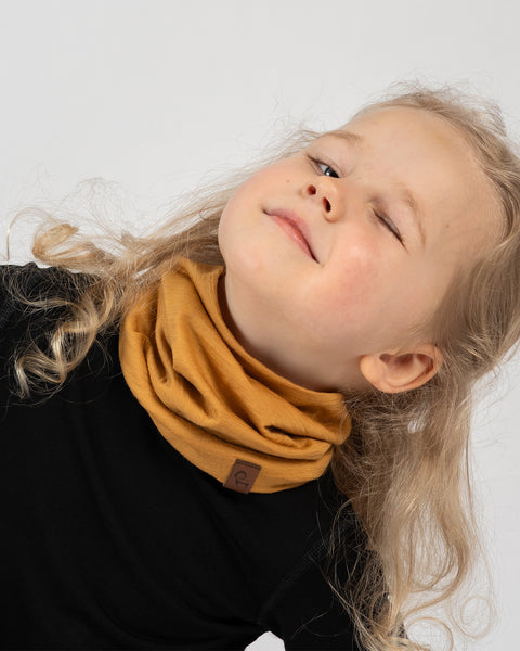 Smiling child wearing mustard yellow merino wool neck gaiter and black base layer top