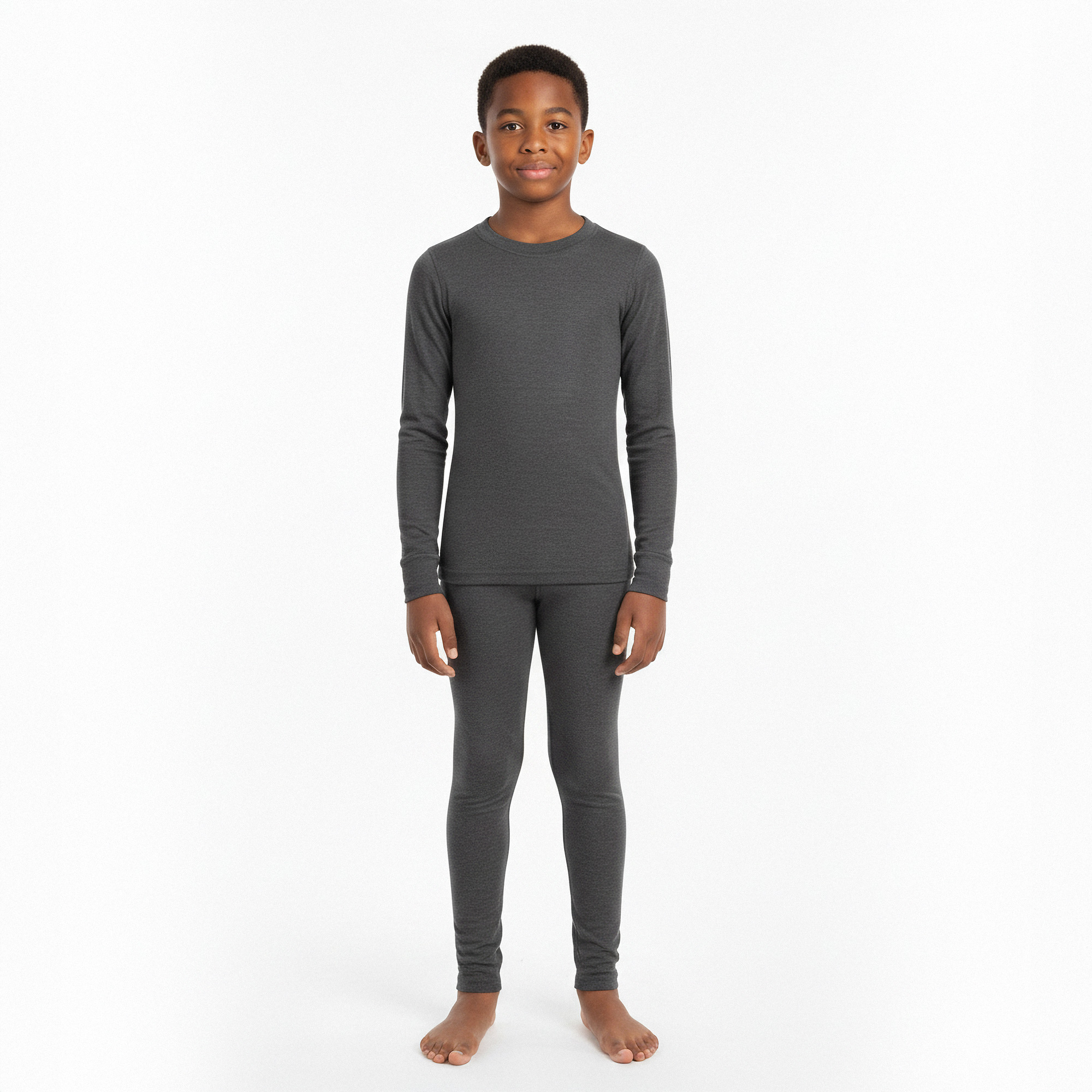 Older boy in gray Merino wool base layer set sitting cross-legged on the floor, neutral background.