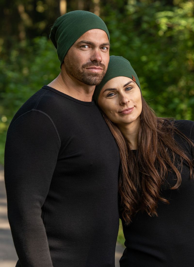Man and woman wearing green beanies and black shirts outdoors with a blurred natural background