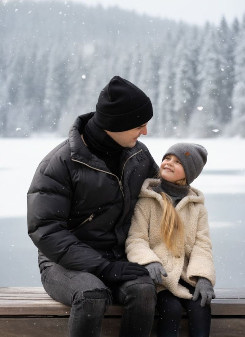 Two people sitting on a bench by a snowy lake with trees in the background.