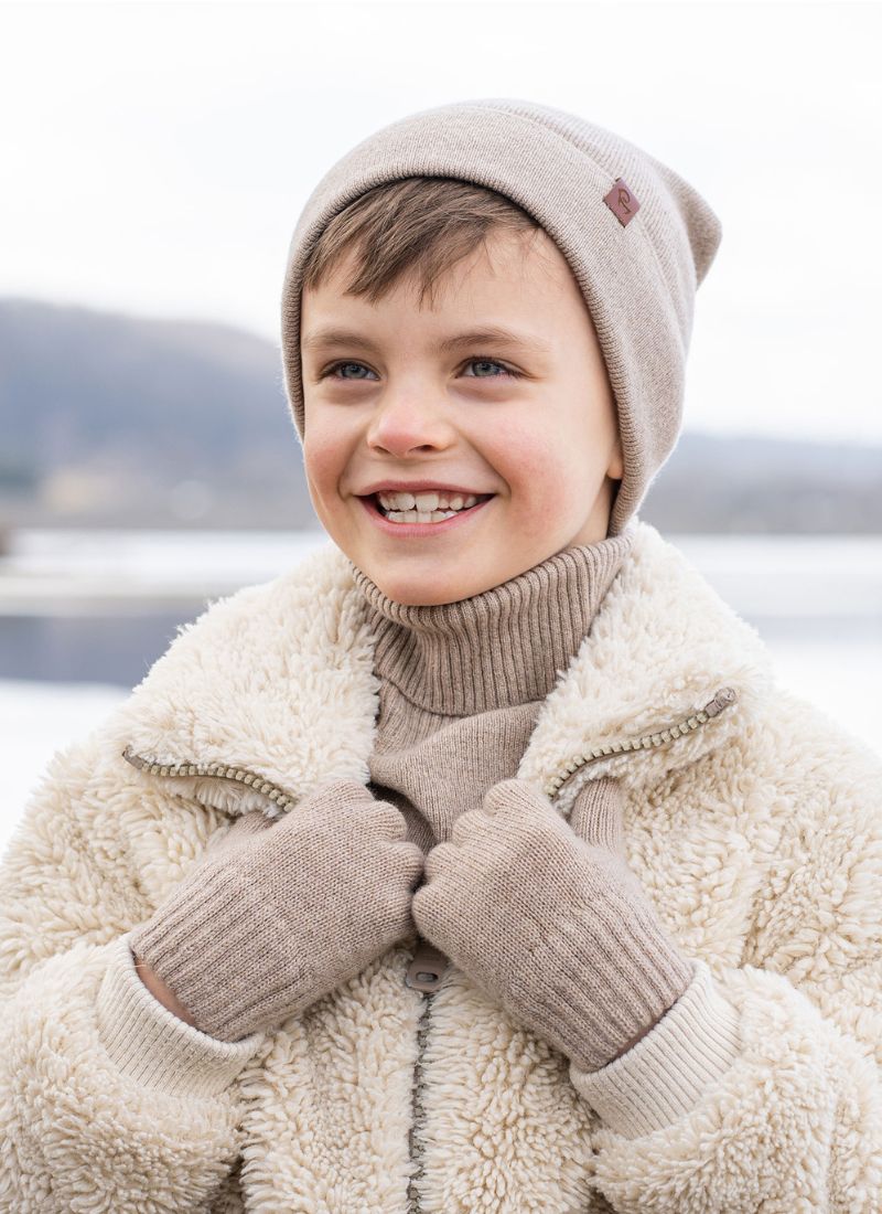 Child wearing a beige coat, hat, and gloves outdoors with a blurred background
