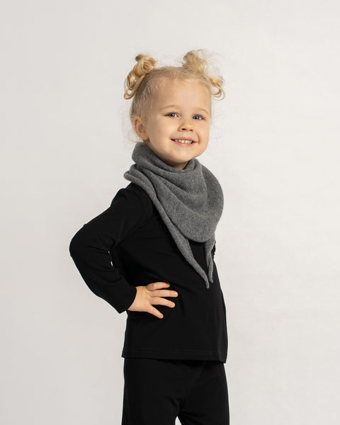 Little girl smiling and posing in a black outfit with a soft grey knit triangle scarf tied around her neck.