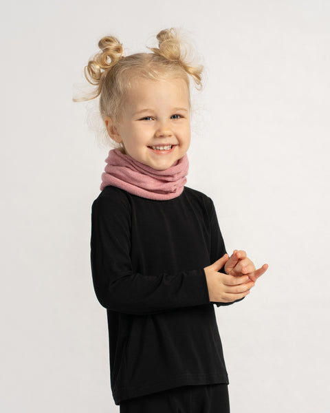 Smiling child wearing a pink knit neck warmer with a black outfit, standing against a light background.