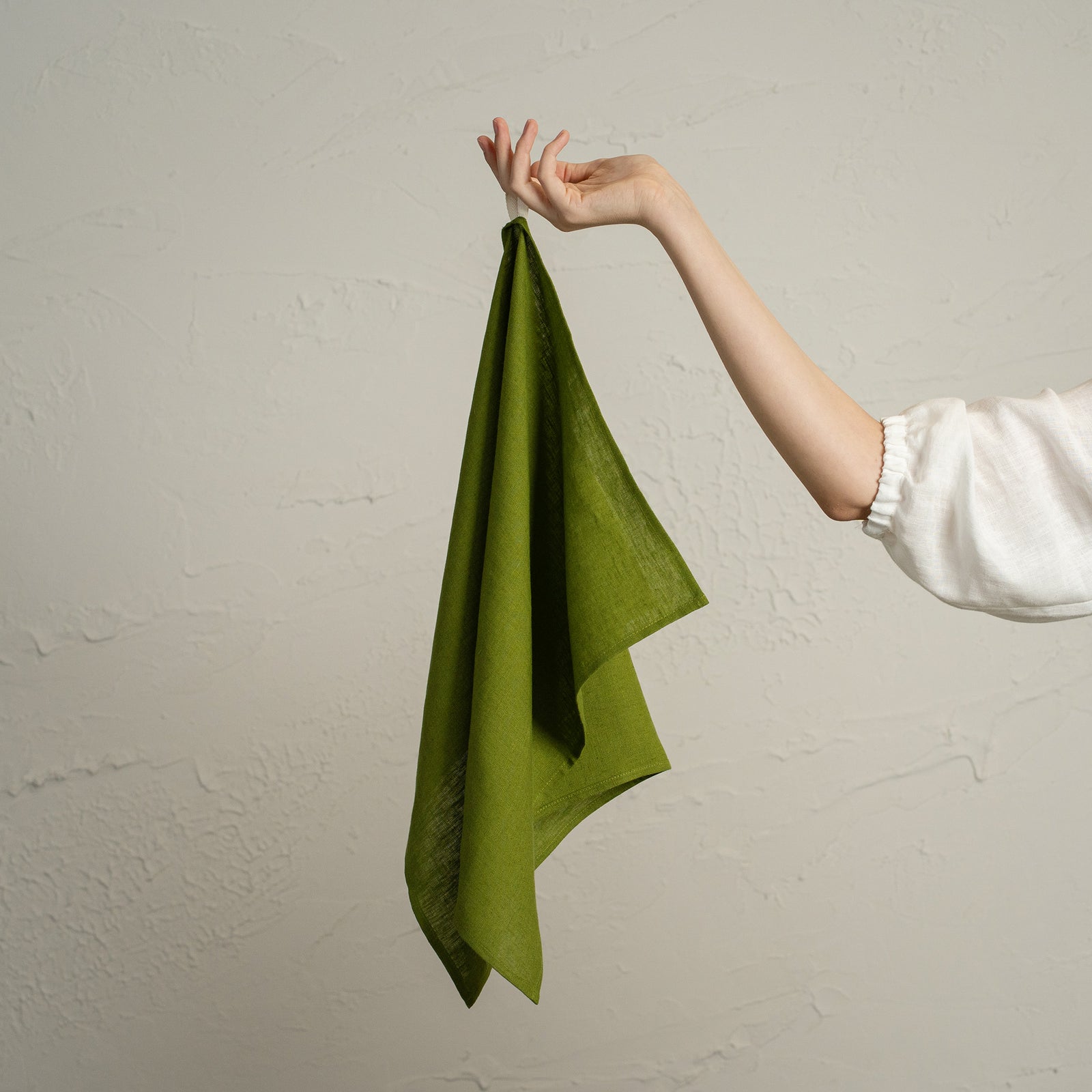 A forest green towel hanging neatly on a wooden peg rack decorated with pinecones, berries, and a small dried orange ornament, against a light textured wall.