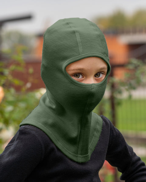 Child wearing a dark green balaclava outdoors with blurred background