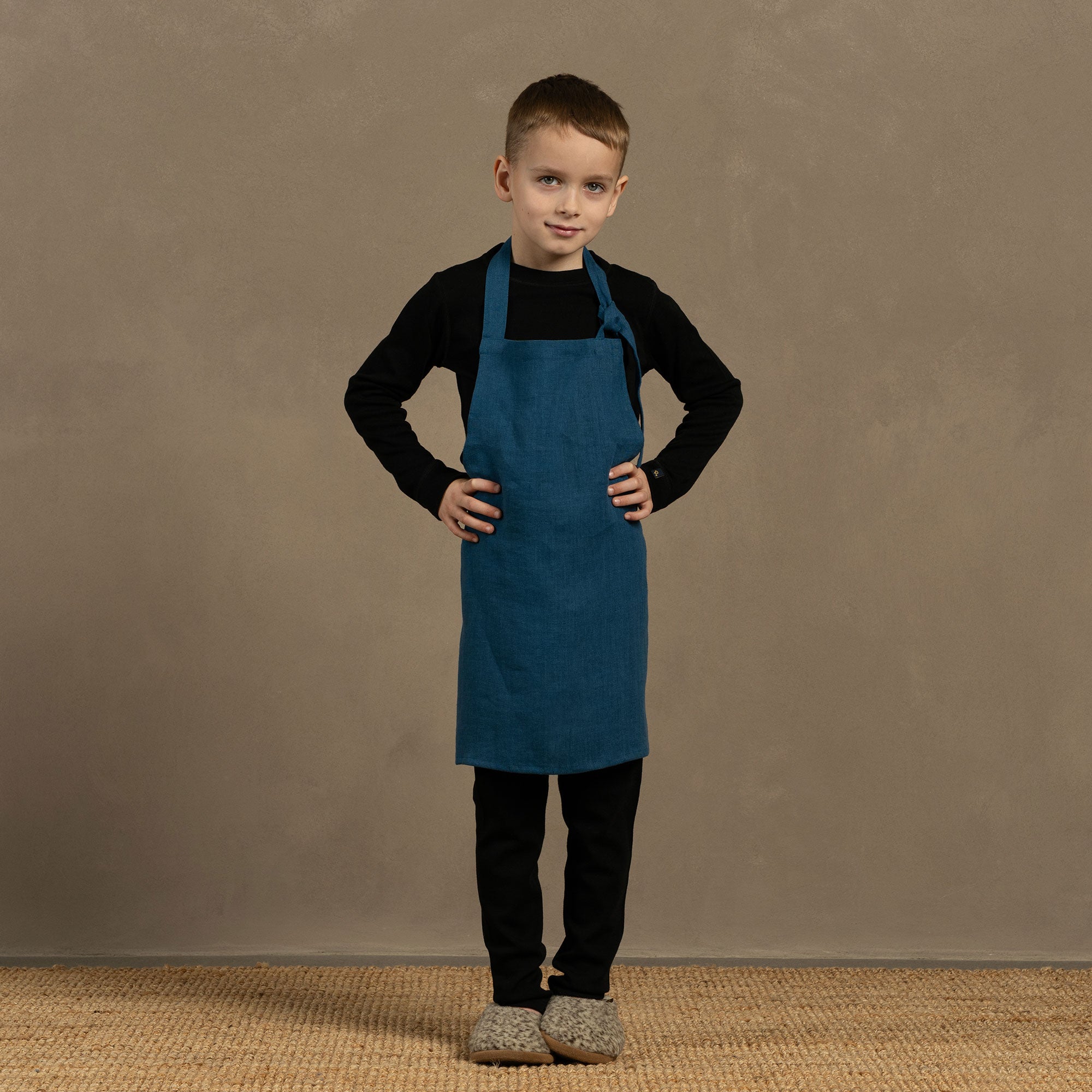 A child wearing a linen apron with leaf dots, standing at a table involved in crafting or baking, with ingredients and baking tools on the table.