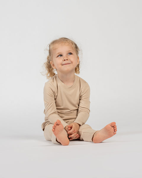 Smiling child sitting on the floor in beige bamboo long-sleeve top and bottoms.