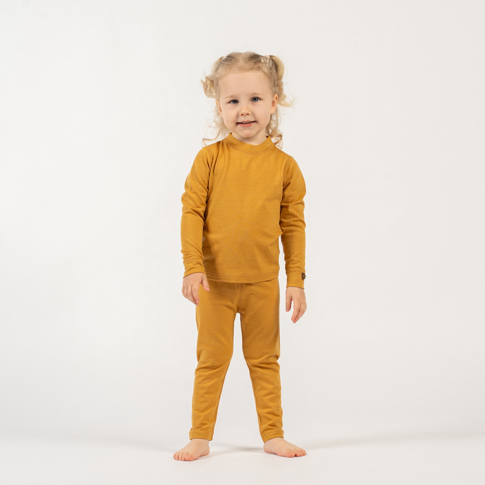 Young girl wearing a menique merino wool yellow long sleeve and bottom set on a white background