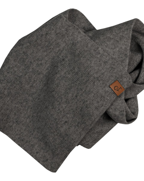 A dark grey knit infinity scarf, with a brown leather tag, is artfully draped against a white background.