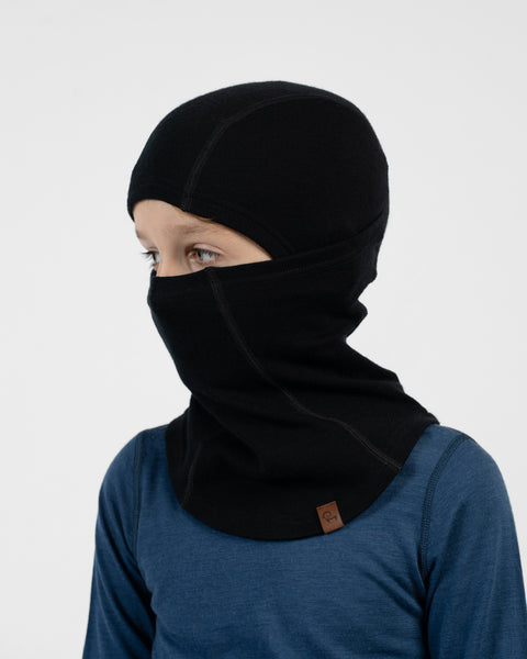 Child in a blue long-sleeve shirt wearing a black balaclava covering their head and pulled up over their nose and mouth.