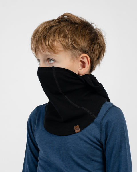 Child in a blue long-sleeve shirt wearing a black neck warmer pulled up over their nose and mouth, with their head uncovered.