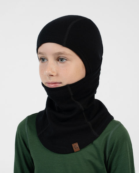 Child in a green long-sleeve shirt wearing a black balaclava covering their head, with the face piece pulled down under their chin.