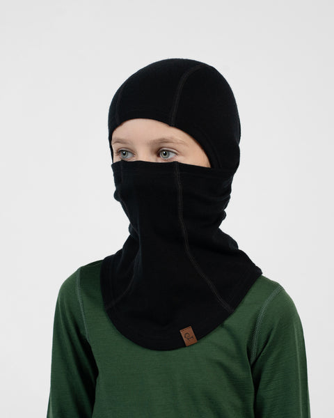 Child in a green long-sleeve shirt wearing a black balaclava covering their head and pulled up over their nose and mouth.