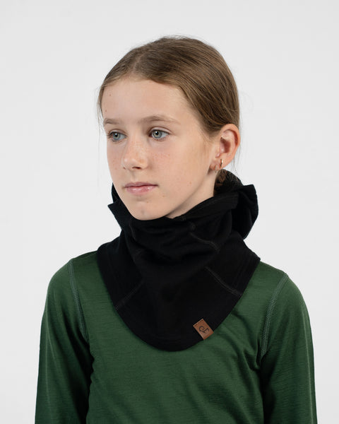 Child in a green long-sleeve shirt wearing a black neck warmer scrunched down around their neck, with their face and head uncovered.