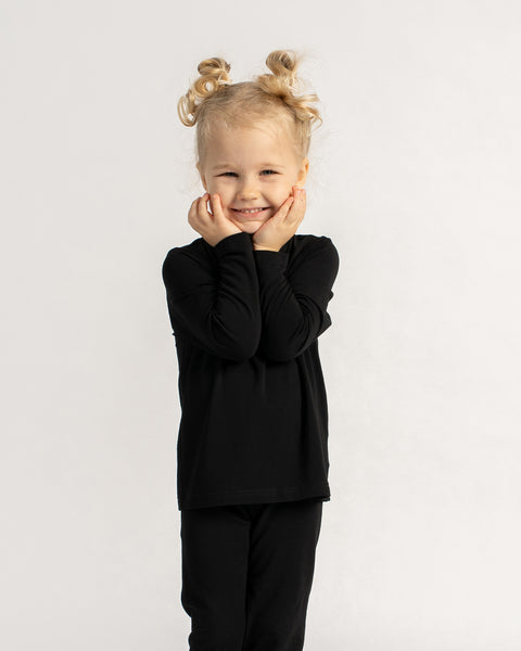 Smiling child wearing black bamboo long sleeve top and leggings, showcasing soft and comfortable kids base layer.