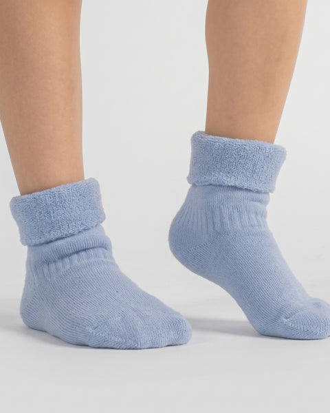 Close-up of bare legs and feet standing on a light background wearing textured light blue crew socks.