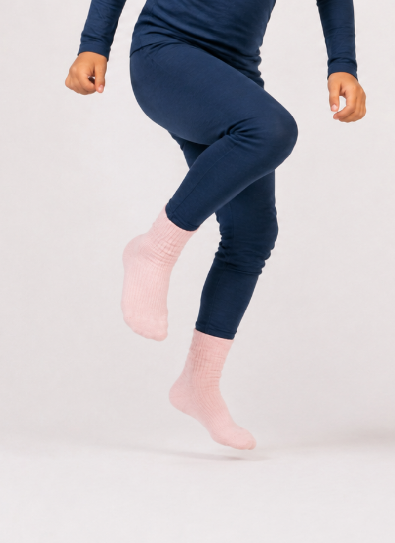 A person from the waist down wearing navy blue leggings and light pink ribbed socks mid-jump against a plain white background.
