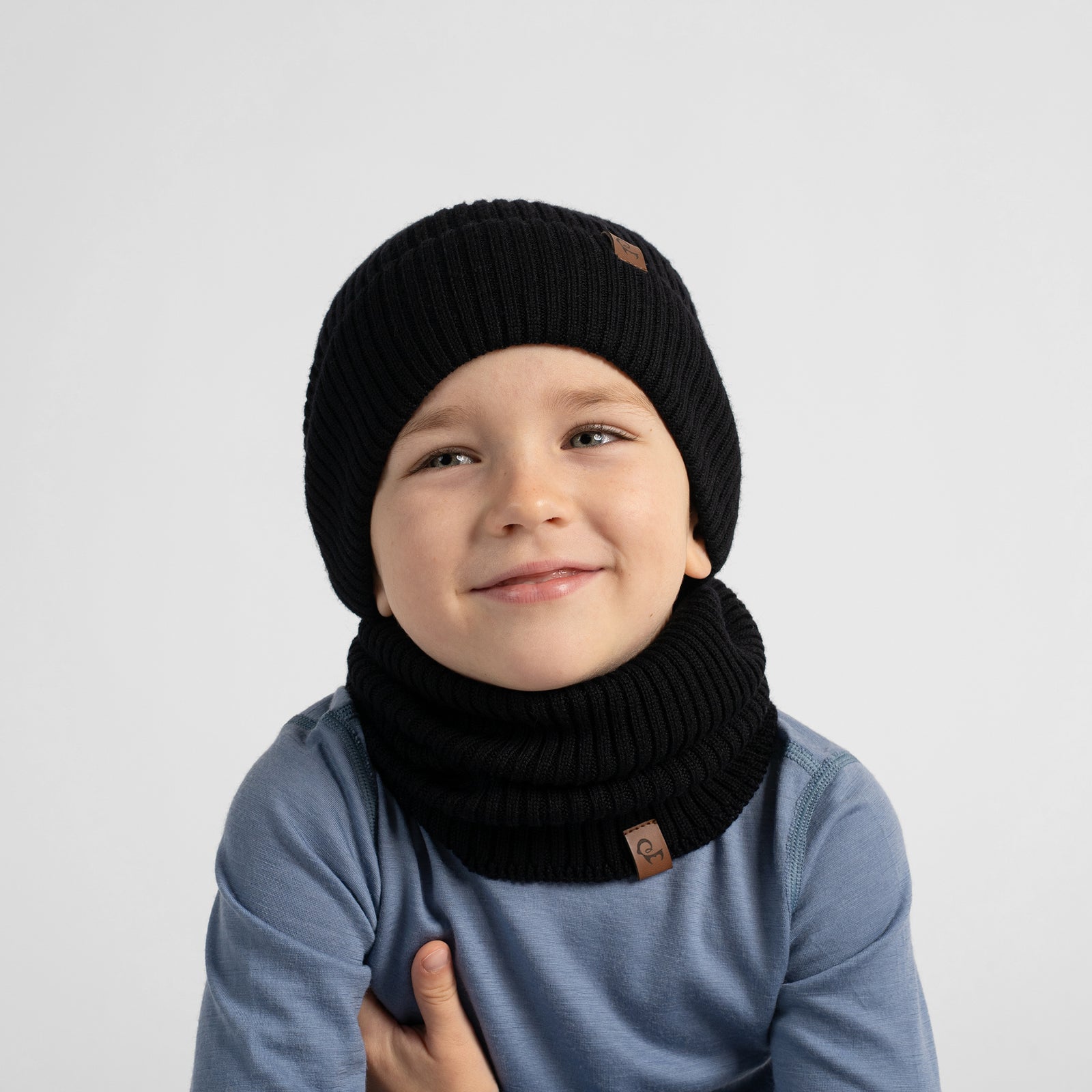 A chest-up portrait of a smiling young girl wearing a dusty rose top, matching beige knit neck warmer, and a light beige beanie.