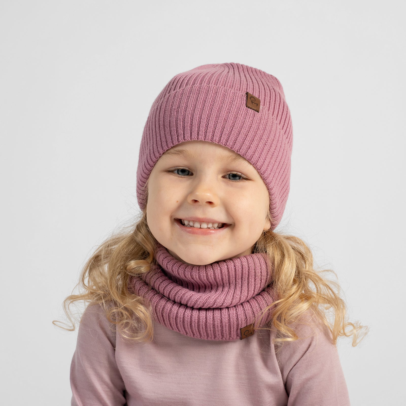 Two children modeling matching knit winter clothing sets against a light gray studio background. The boy wears a blue beanie and matching neck warmer with dark navy long-sleeve top and pants.