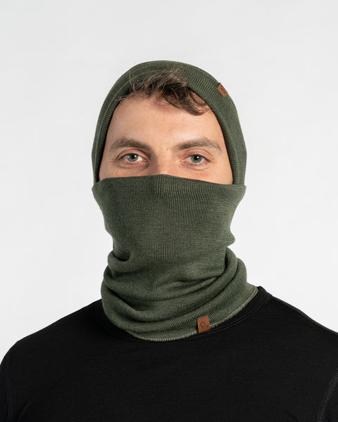 Man wearing a dark green menique merino wool knitted neck gaiter and beanie on a white background