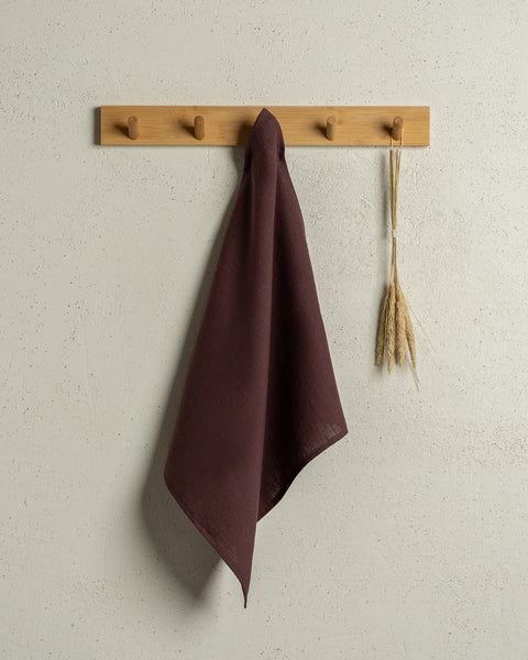 The menique square linen dish towel in color shadow purple hanging on a wooden rack on a wall.