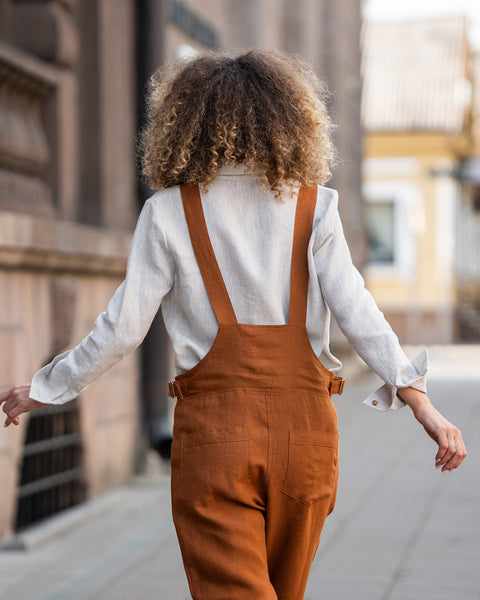 Woman with curly hair standing in a street and wearing Linen Pinafore Jumpsuit Nicci Almond Brown
