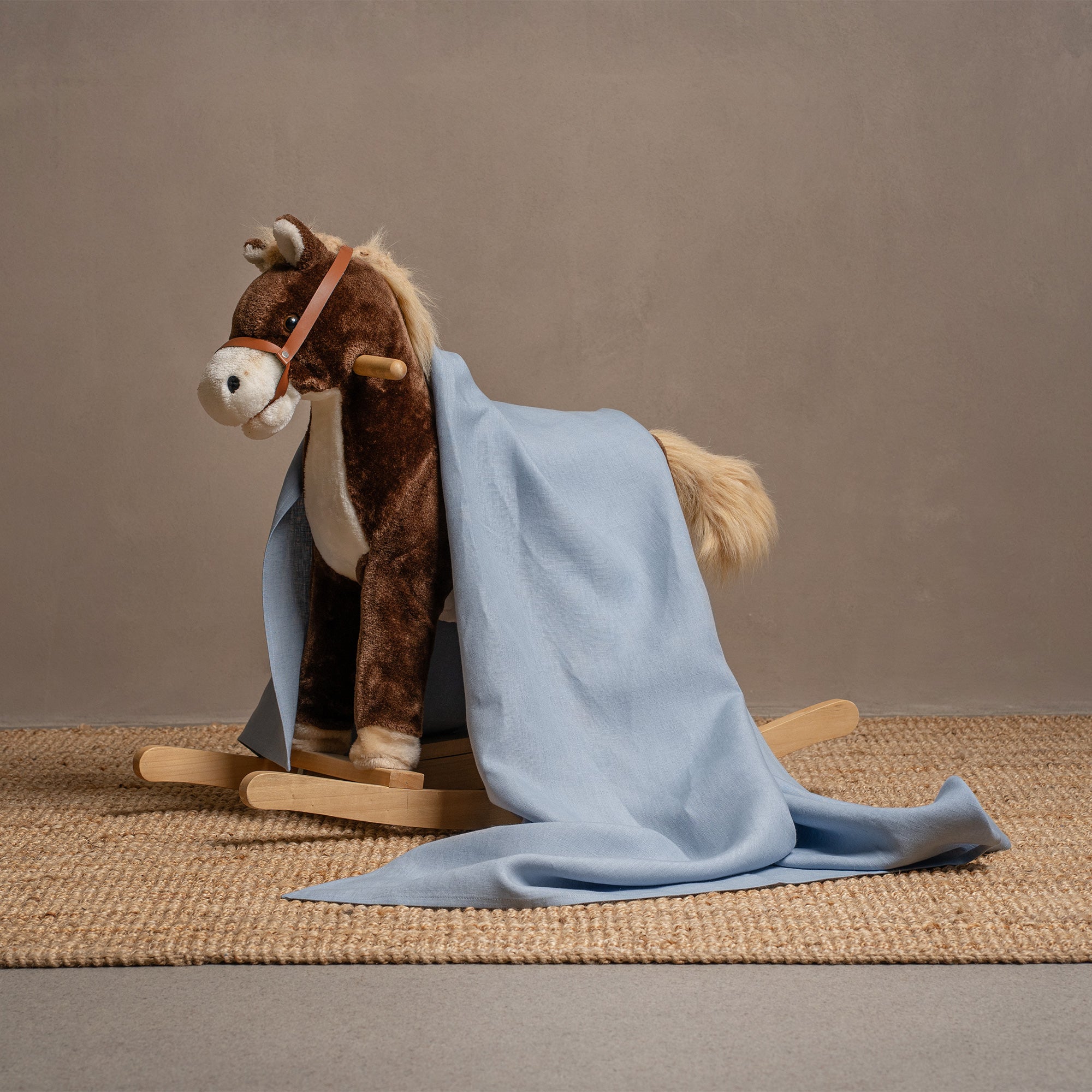 Baby sleeping in a white crib under a mustard yellow linen blanket, on a natural brown woven rug.
