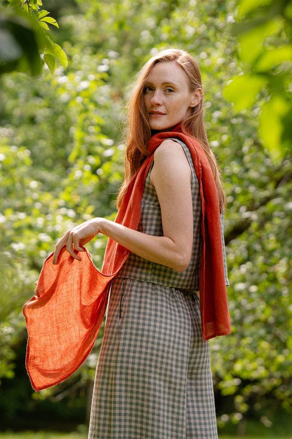 A woman wearing a checkered outfit and an orange scarf poses with their hands on the scarf.



