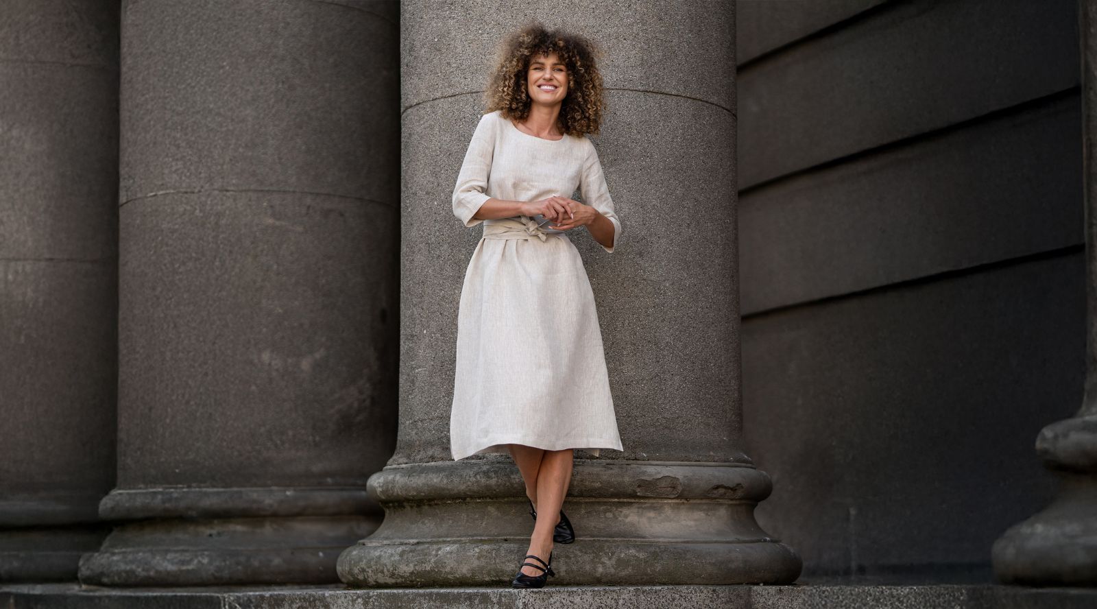 Woman in a white dress standing on stone steps with columns in the background