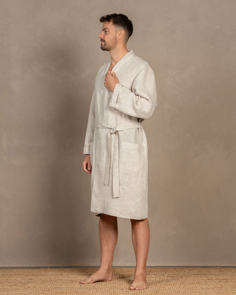 A man, turned to the side, visible in full height, holding the bathrobe collar with one hand, while the other hangs loosely. The bathrobe is knee-length.