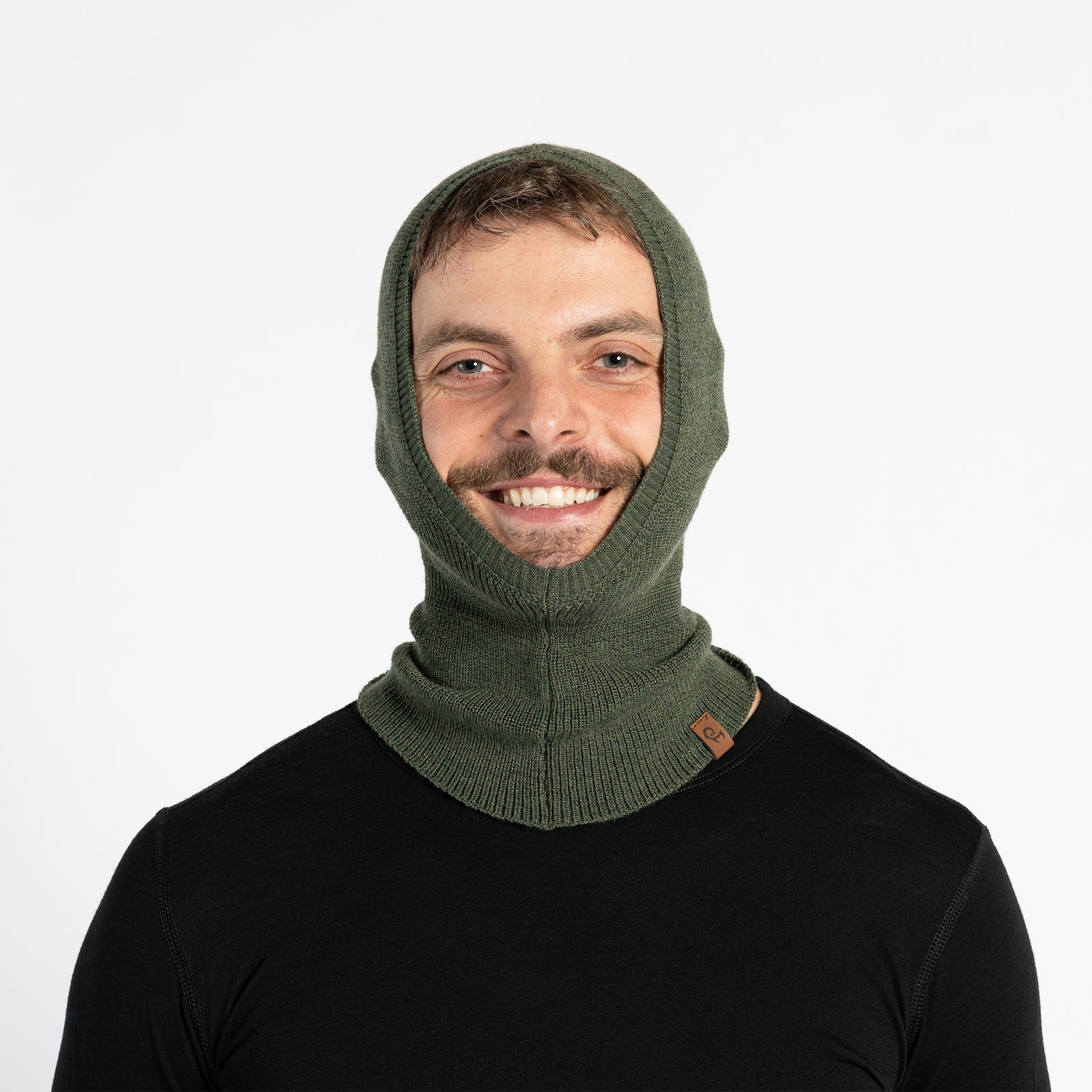 Smiling man on ski slopes wearing a dark gray Merino wool liner balaclava under a blue ski jacket and goggles.