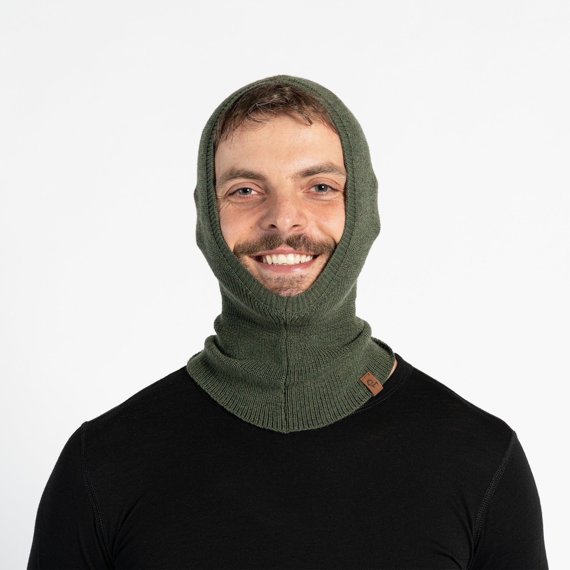 Smiling man on ski slopes wearing a dark gray Merino wool liner balaclava under a blue ski jacket and goggles.