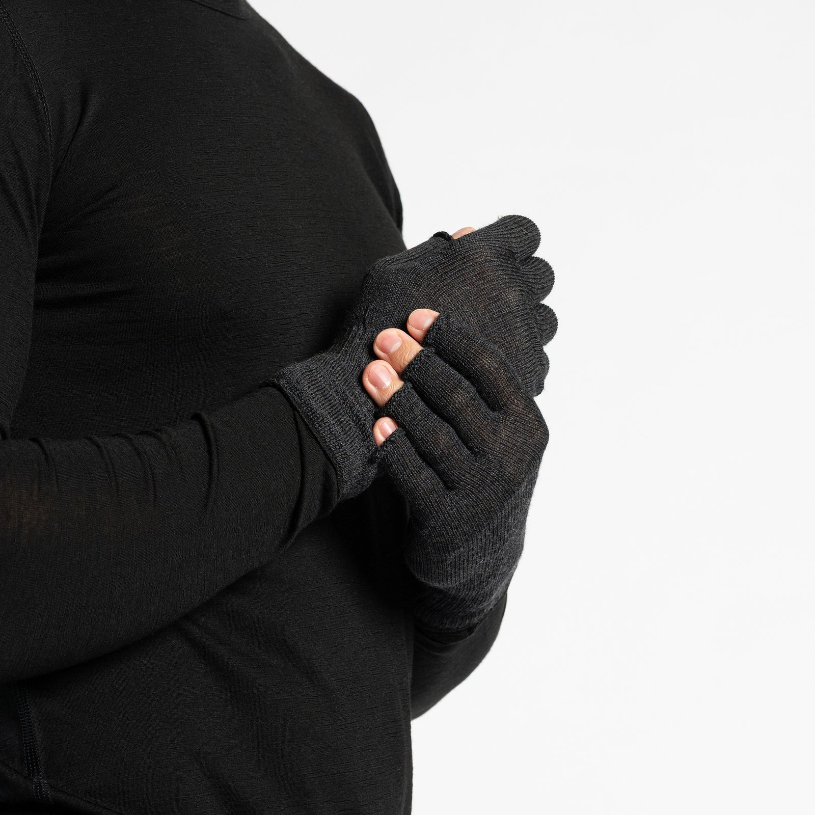 A person wearing a black long-sleeved shirt is shown from the chest up, putting on dark green fingerless gloves. The background is white.
