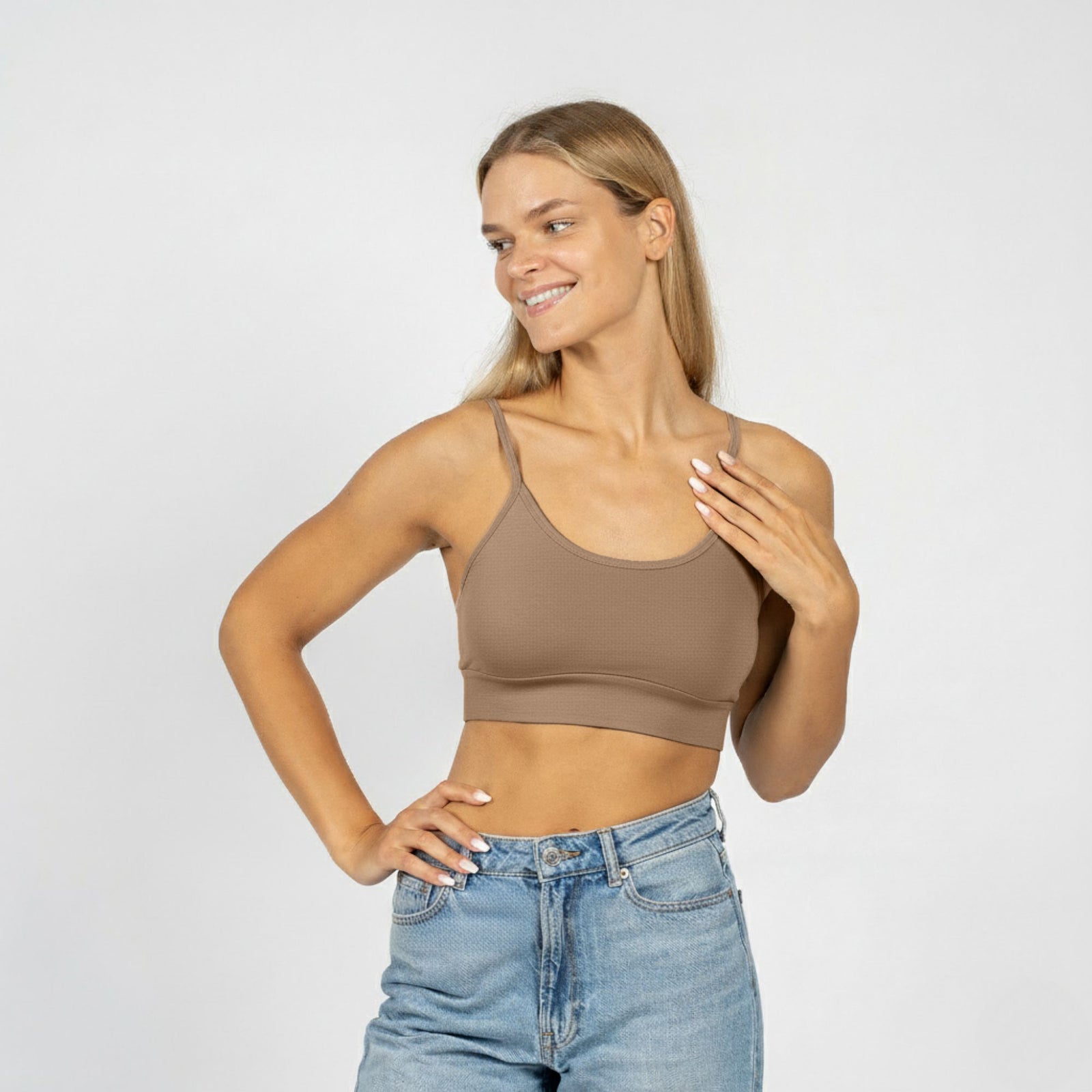 Woman wearing a brown crop top and blue jeans on a plain background