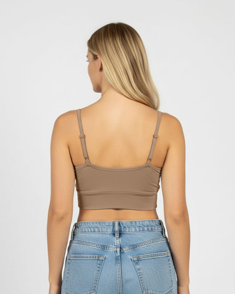 Woman wearing a beige crop top and blue jeans on a plain background