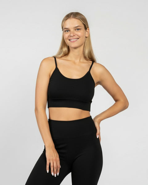 Woman wearing a black sports bra and leggings on a light gray background